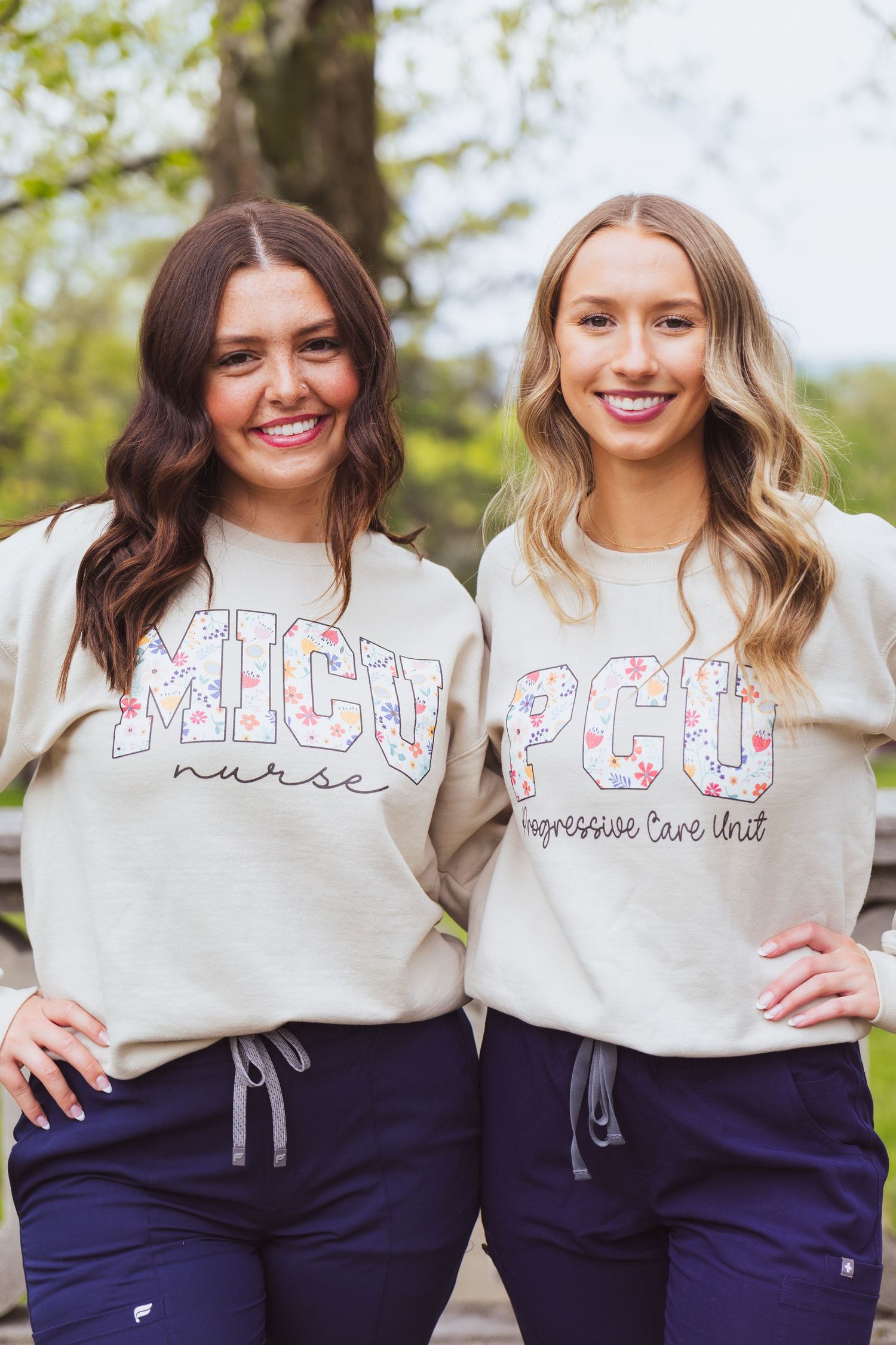 Two healthcare workers in matching MICU sweatshirts and navy scrub pants pose outdoors.