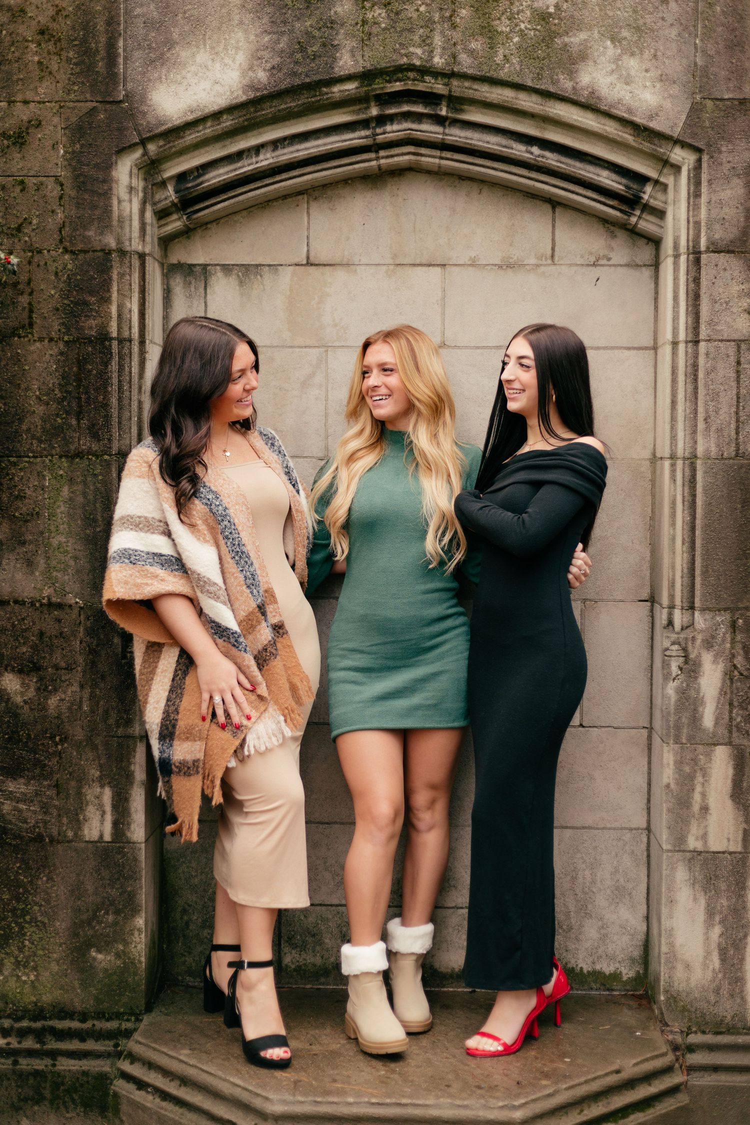 Three friends strike a casual pose in front of a gothic stone alcove wearing trendy fall outfits.