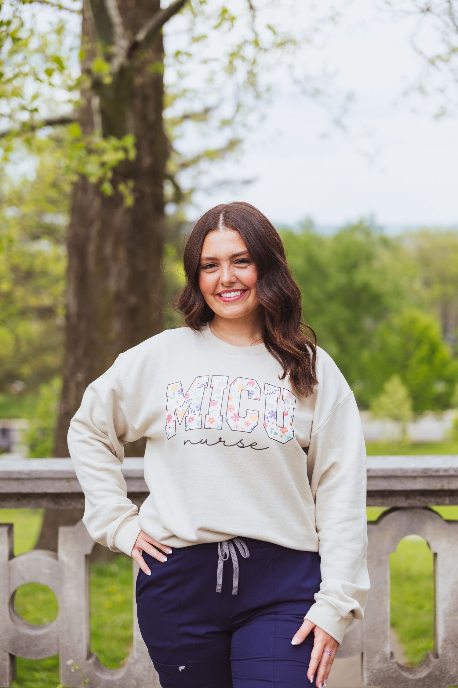 A person wearing a cream-colored sweatshirt with 'Michigan' text and navy pants poses outdoors by a stone railing.