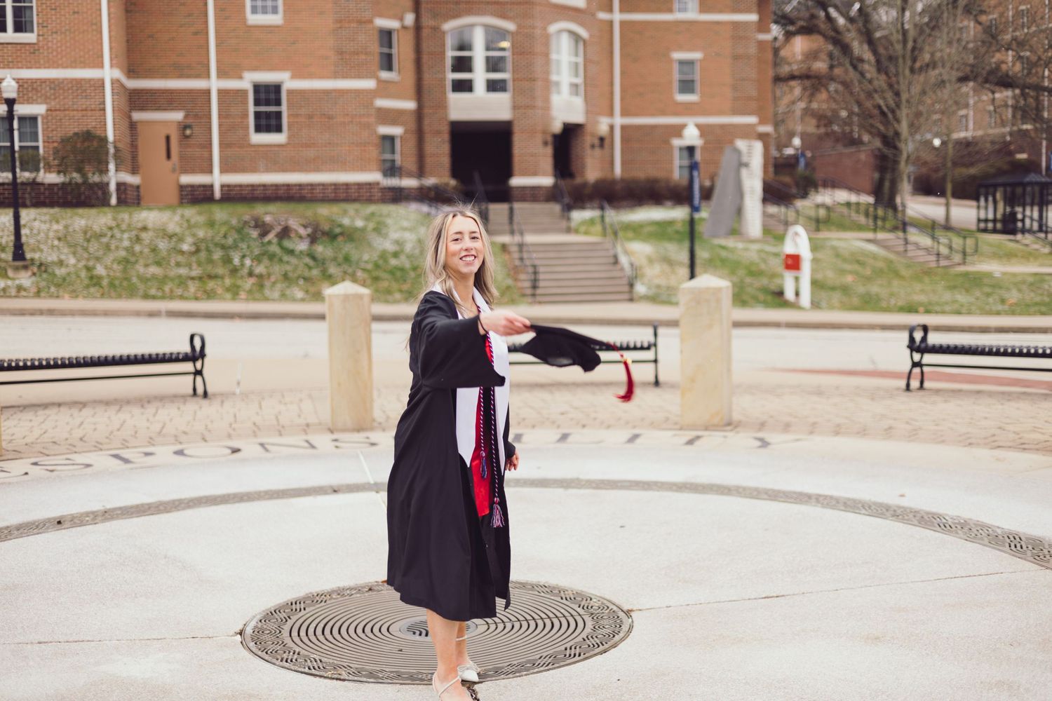 Graduate in black gown posing on circular brick pattern.