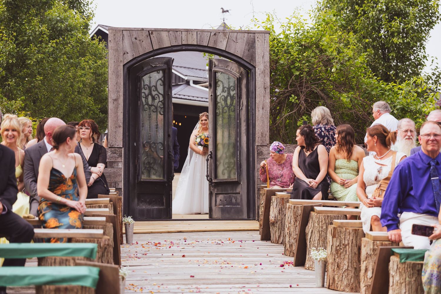 Outdoor wedding venue with rustic wooden pavilion and log benches surrounded by green trees.