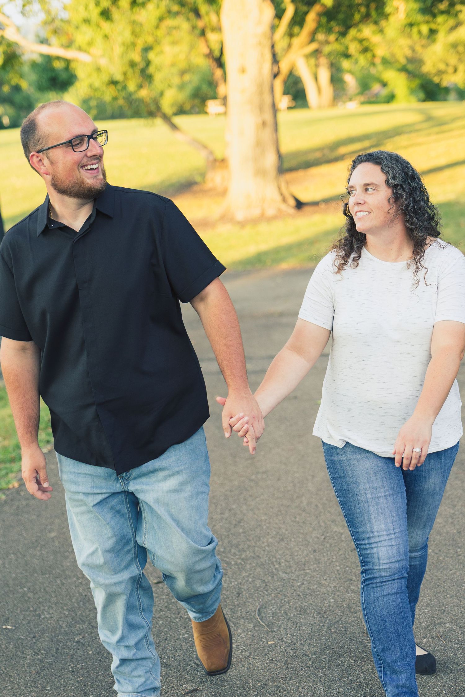 Happy couple holding hands and walking together on a park path surrounded by lush green trees.