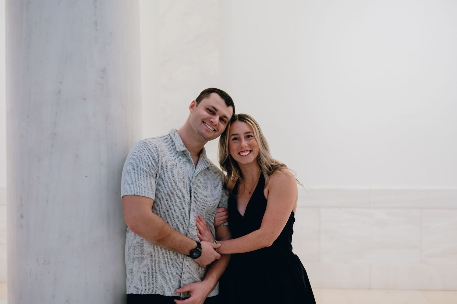 Candid couple portrait showing affection against white wall background.
