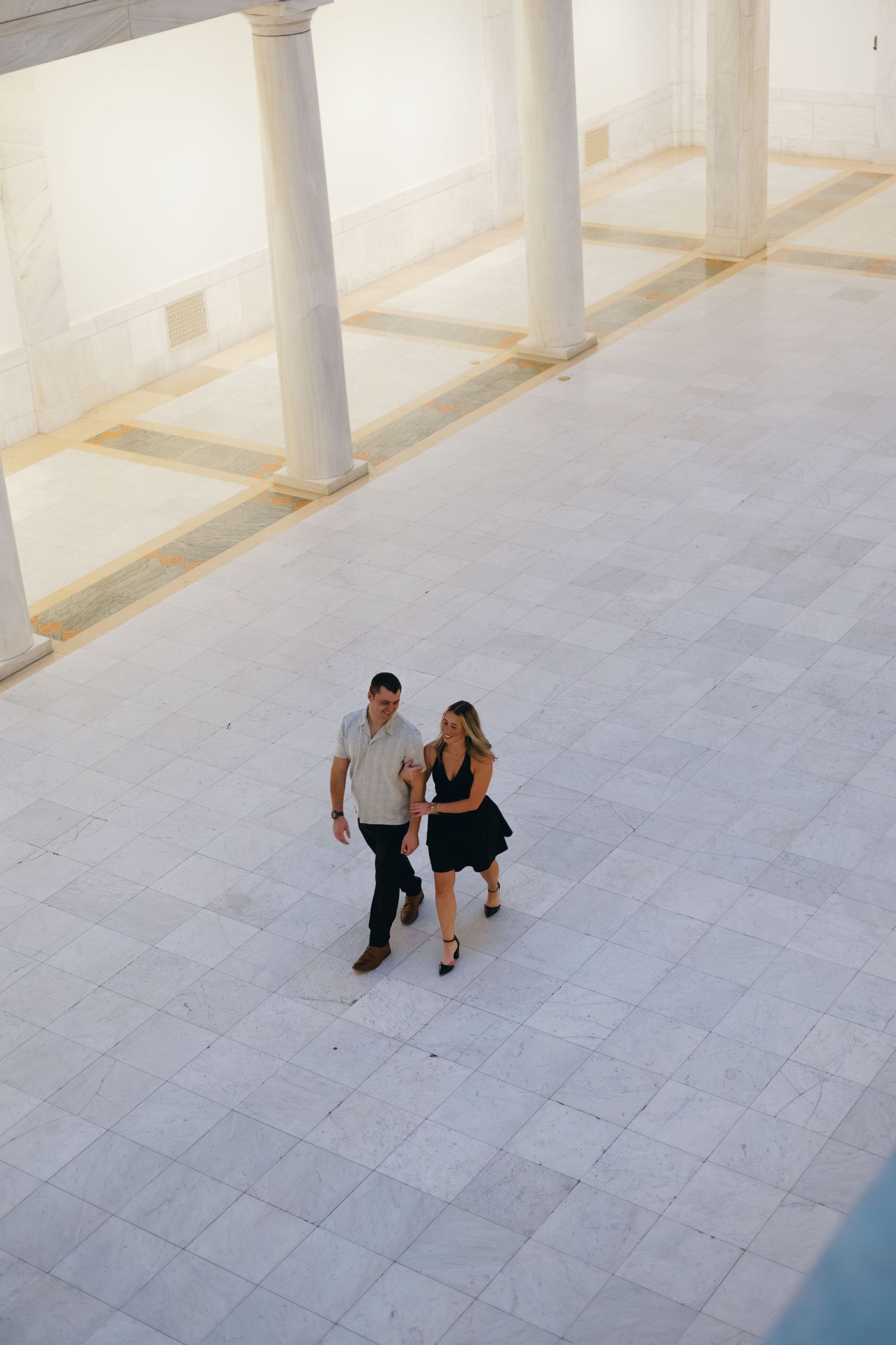 Aerial view of couple walking together in bright architectural space with columns.