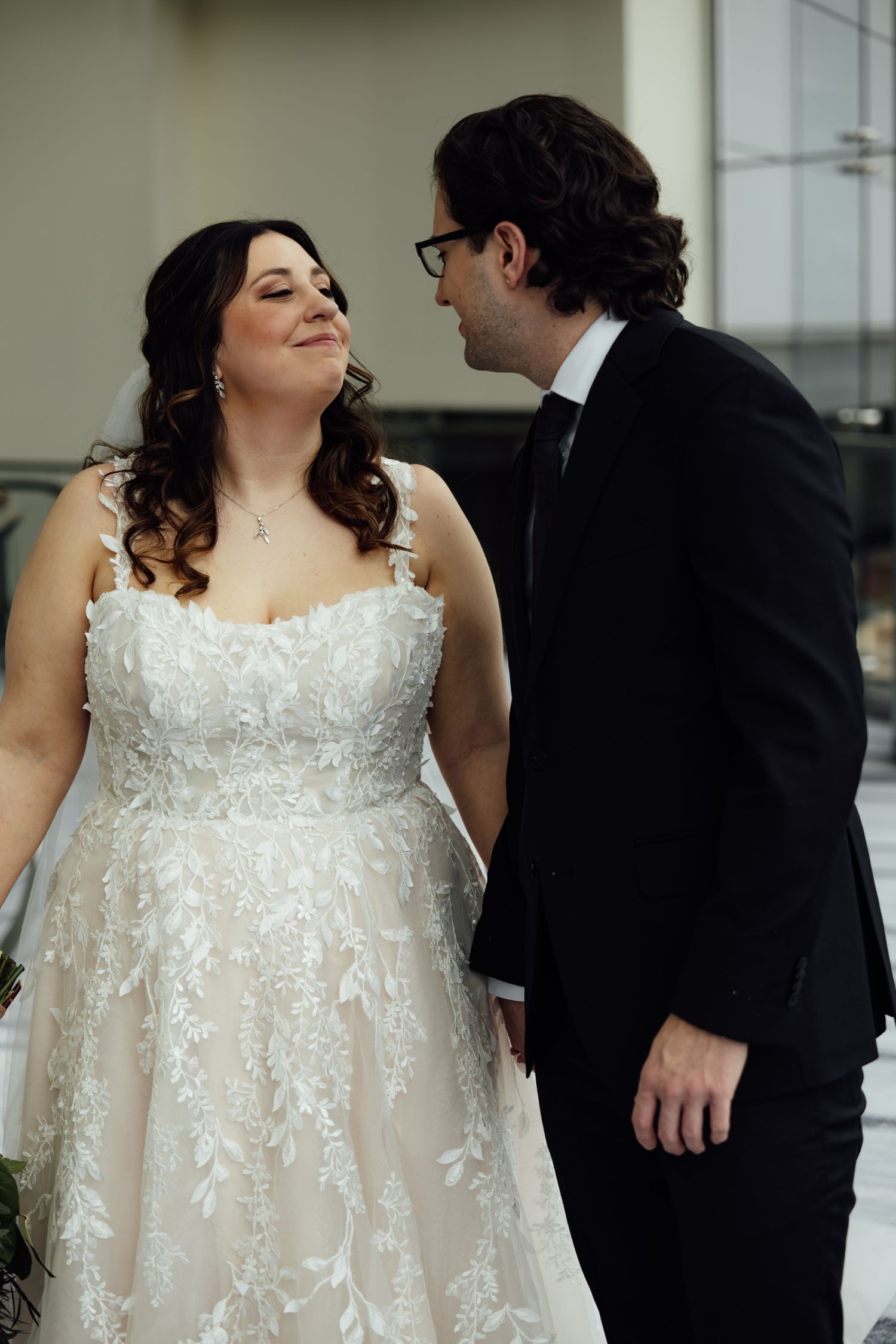 Bride in lace gown and groom in black tuxedo share a romantic moment during their wedding day.