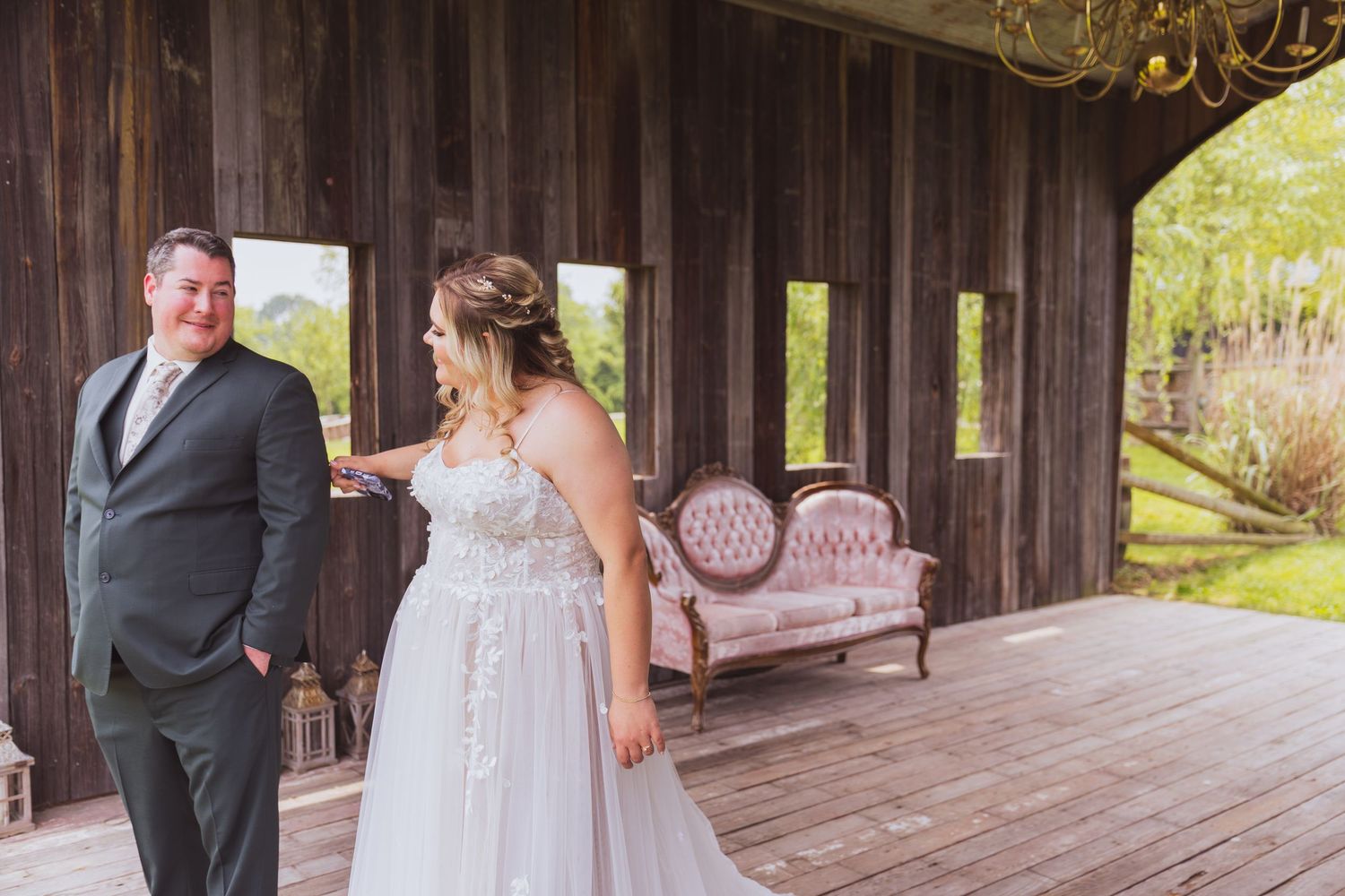 A couple shares a romantic first look on a rustic wooden porch decorated with a vintage pink sofa.
