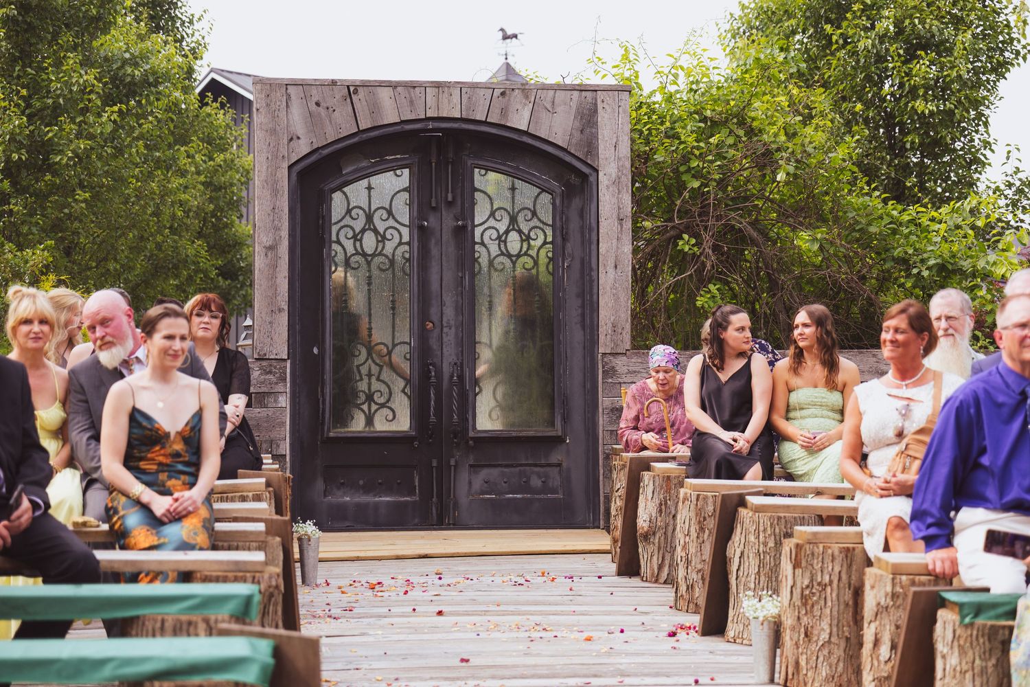 A rustic outdoor wedding ceremony setup with wooden log benches and an elegant iron door backdrop.