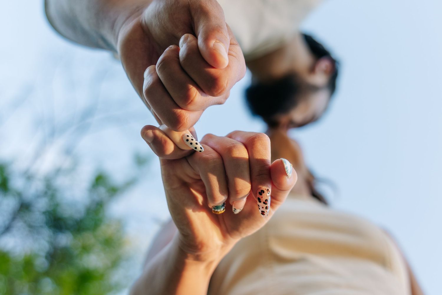 Close-up of couple holding hands with decorative rings against a blue sky backdrop.