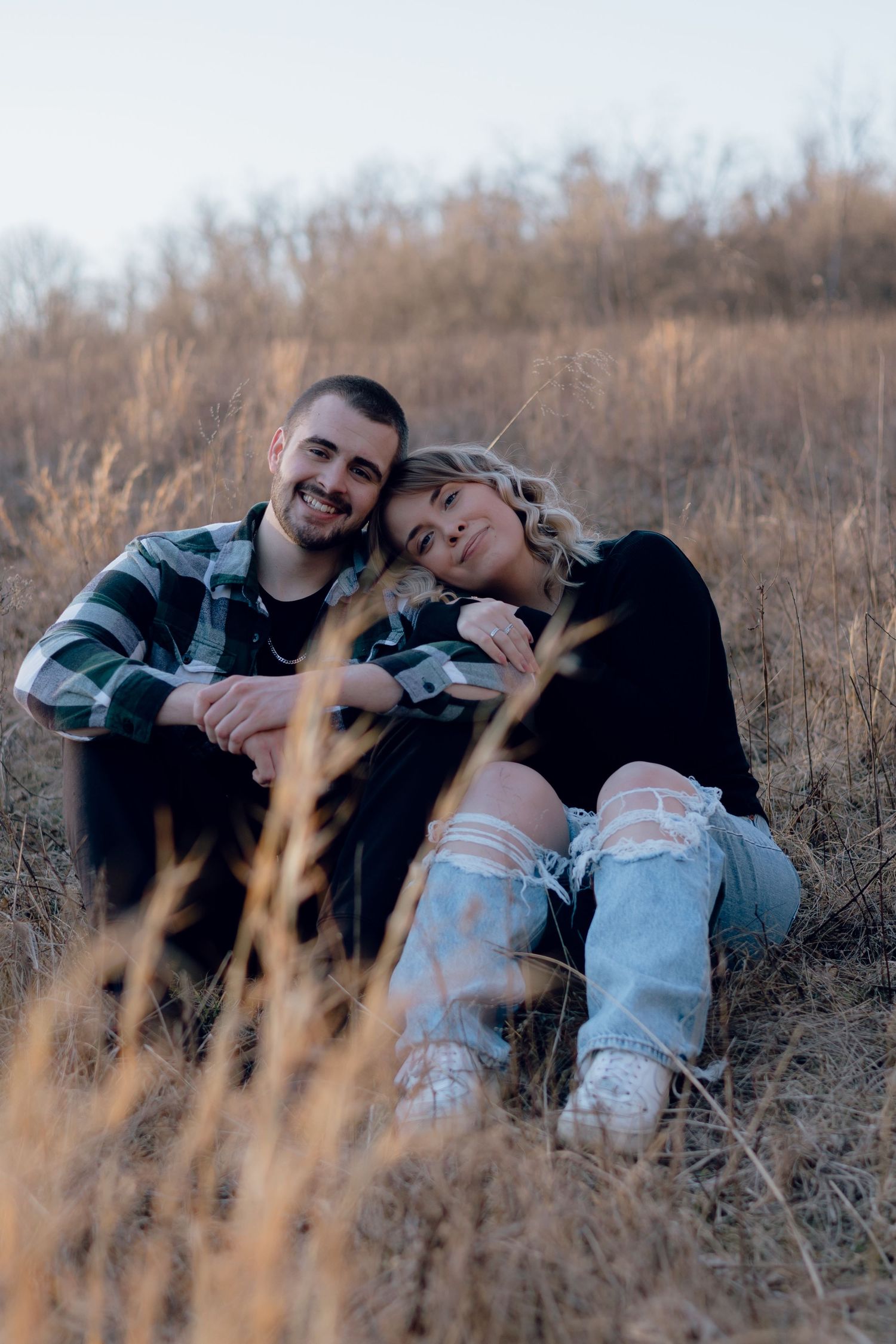 Couple relaxing in field of dried grass during golden hour.