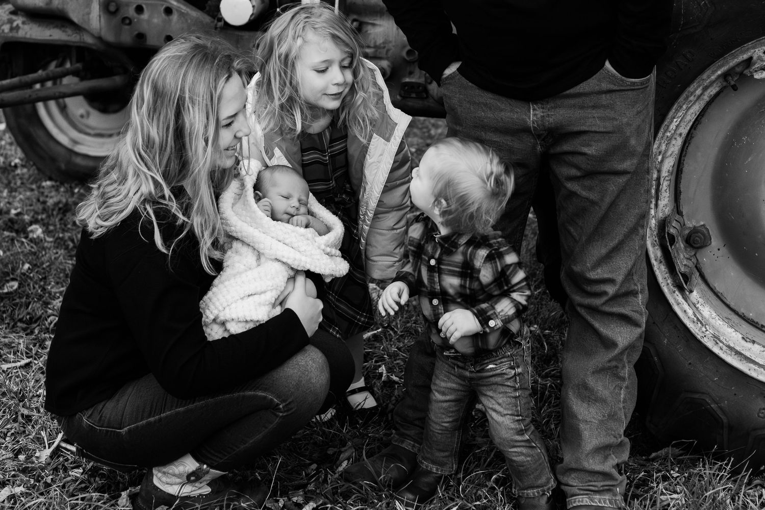 Black and white family photo of group gathered around large tractor wheel outdoors.