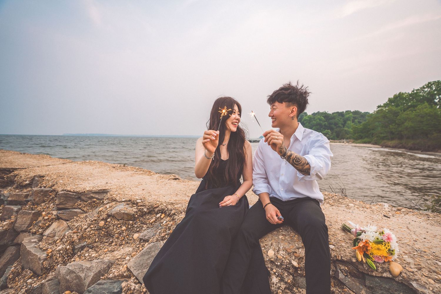 A couple enjoying drinks together on a rocky beach at sunset.