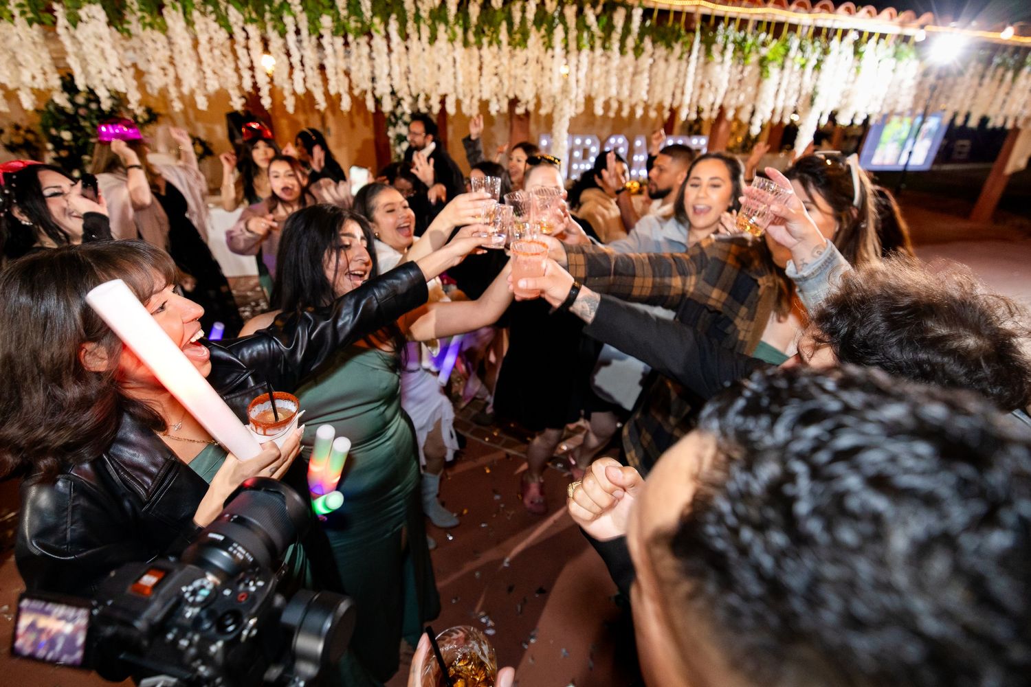 Wedding guests dance and celebrate energetically on a crowded dance floor beneath twinkling string lights.