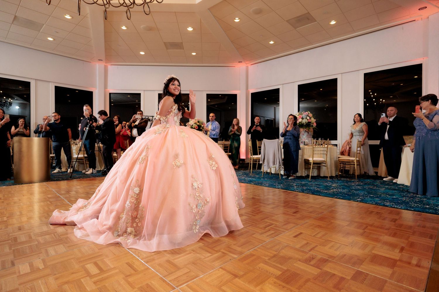 Large ballroom with parquet flooring and pink lighting for a formal celebration.
