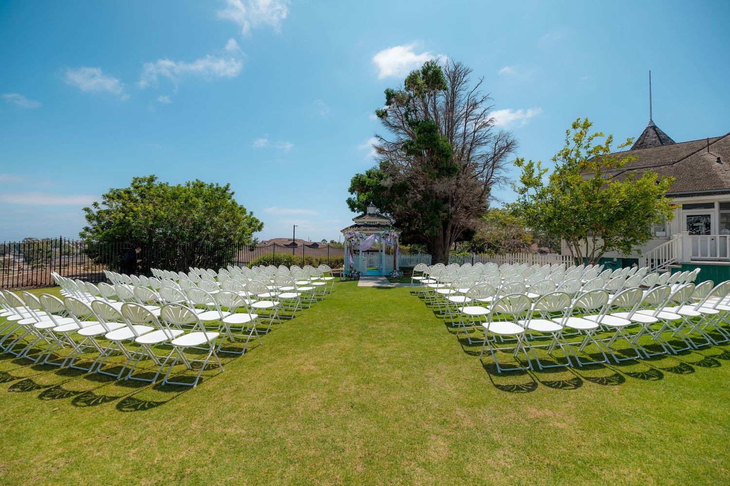 White folding chairs arranged in curved rows on a grassy lawn for an outdoor ceremony under blue skies.