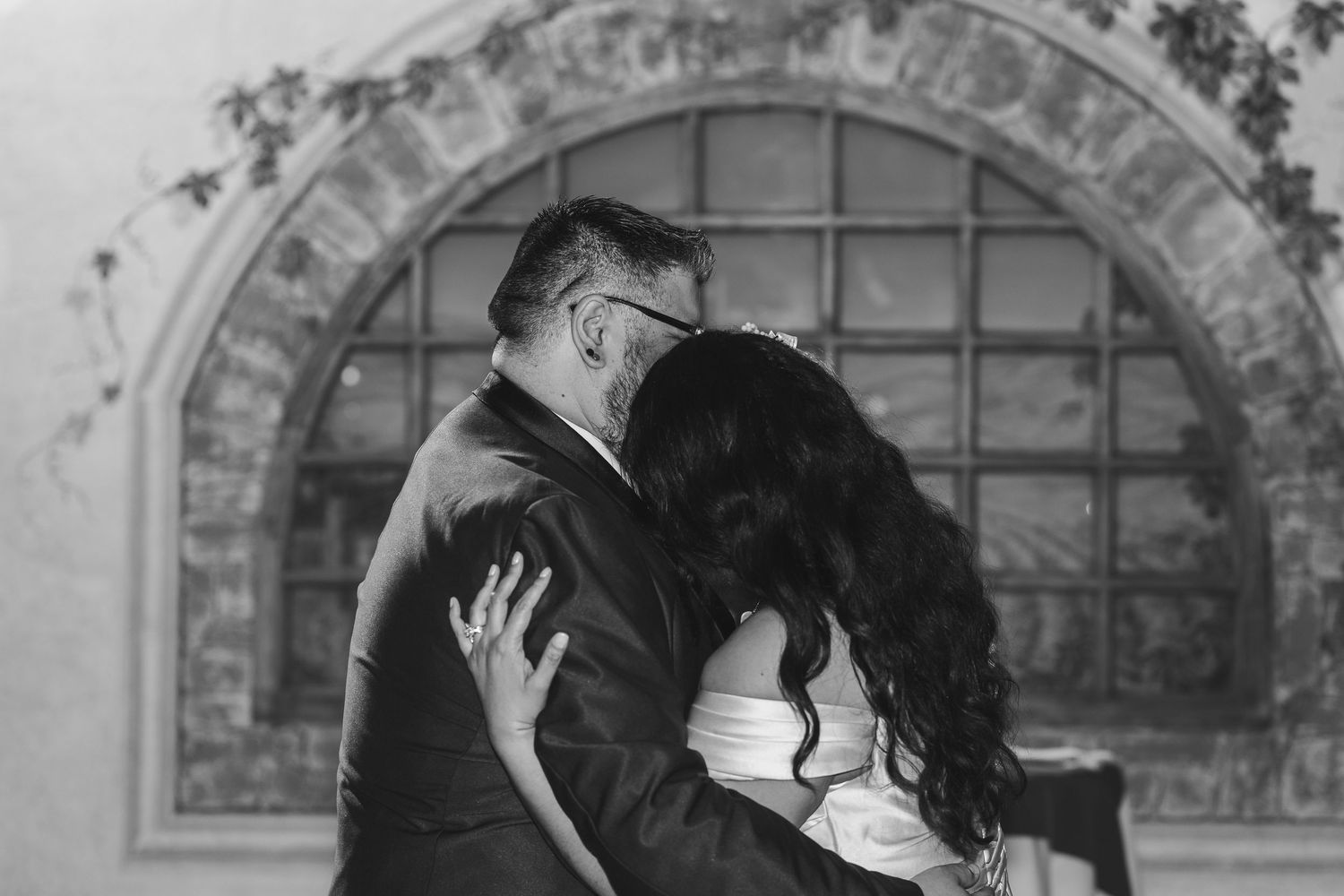 A series of black and white photos showing a couple embracing and kissing in front of an arched window.