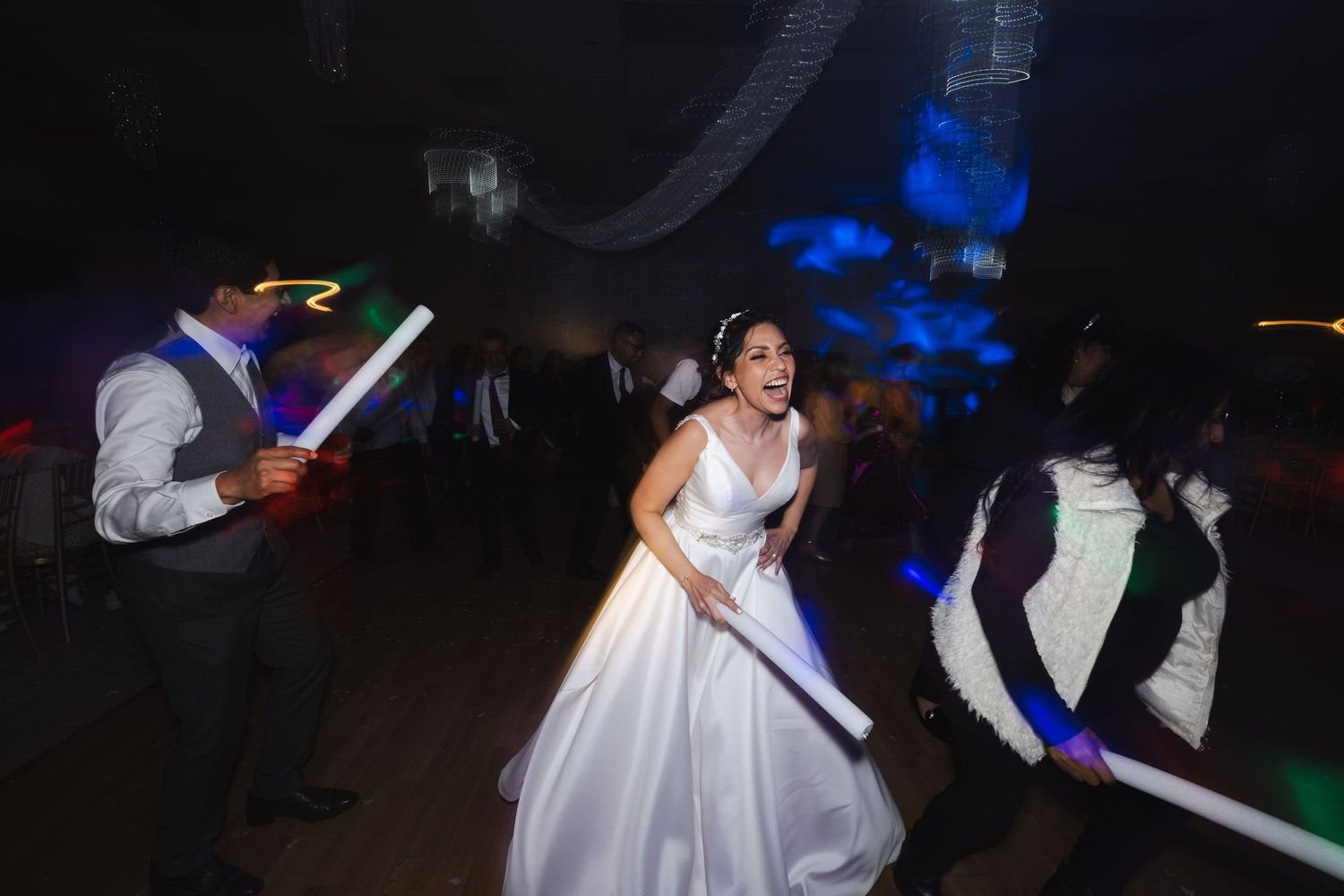 Wedding guests wave colorful lightsabers during a nighttime celebration on the dance floor.