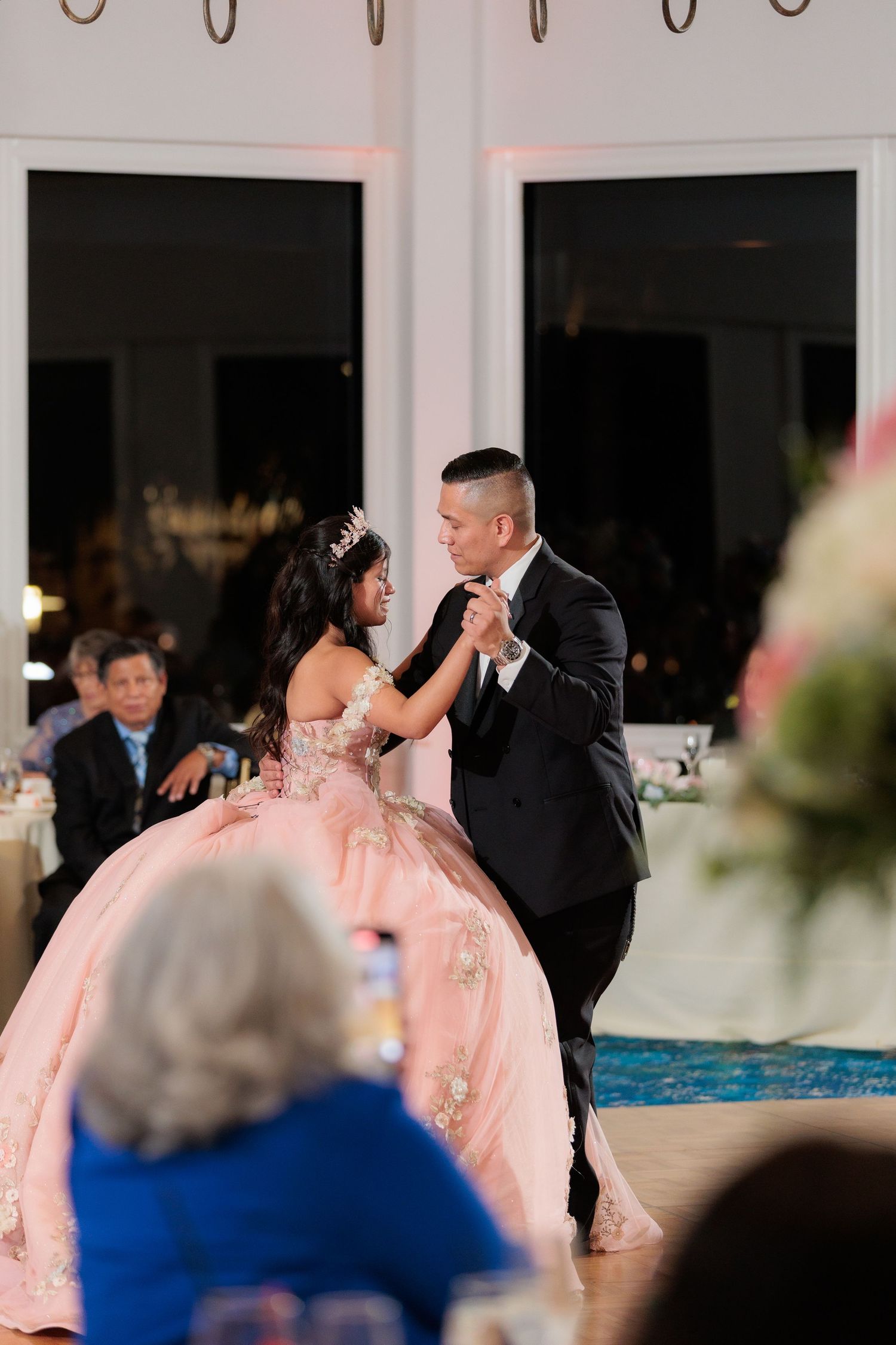 Couples dancing together at an elegant indoor reception with pink decor and ambient lighting.