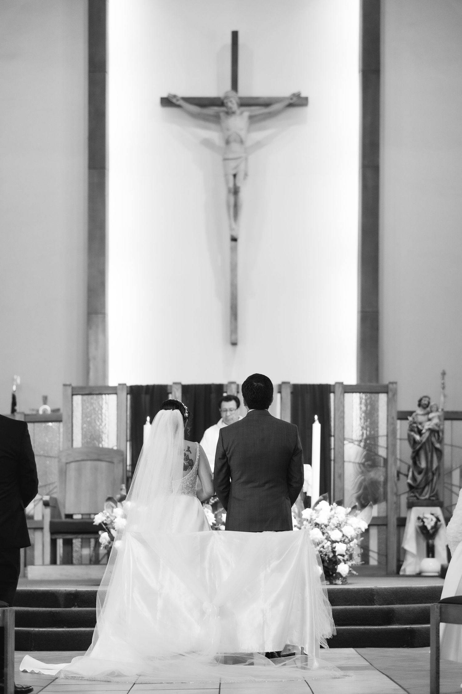 A black and white photo shows a couple kneeling at the altar during a traditional Catholic church wedding ceremony.