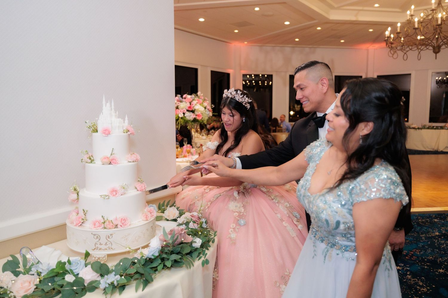 Wedding reception venue with pink decor, floral arrangements, and a white tiered cake on display.
