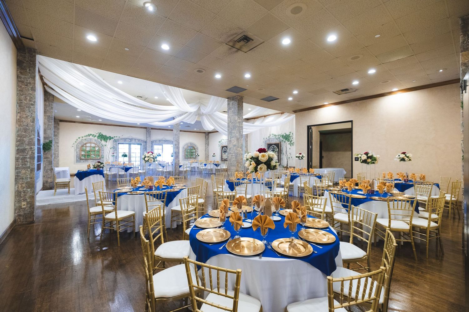 Wedding reception venue with elegant blue tablecloths and gold chiavari chairs set for dining.