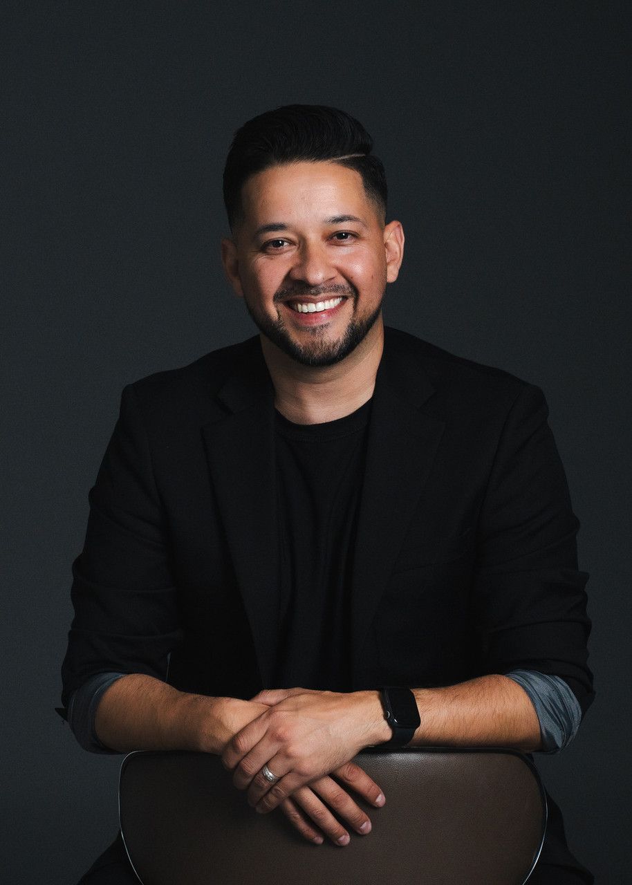 Professional headshot of photographer in black blazer against dark background.