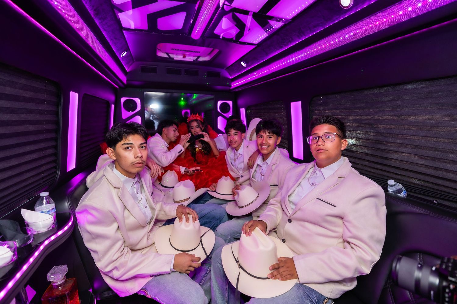 A group of people dance and socialize in a nightclub with purple lighting and dark interior decor.