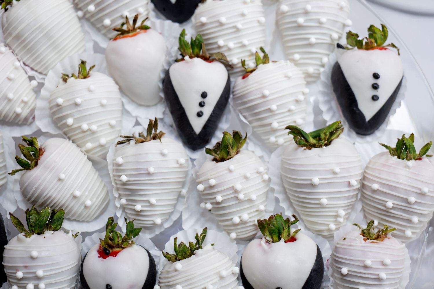White chocolate covered strawberries decorated as wedding tuxedos and bridal dresses on display.