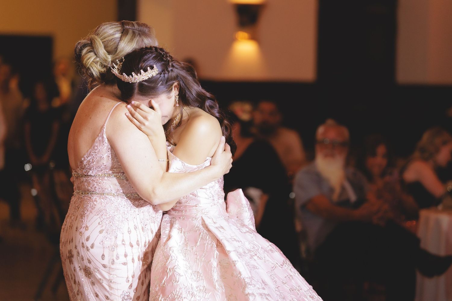Wedding guests dance together at a reception in a dimly lit ballroom with warm lighting and romantic atmosphere.
