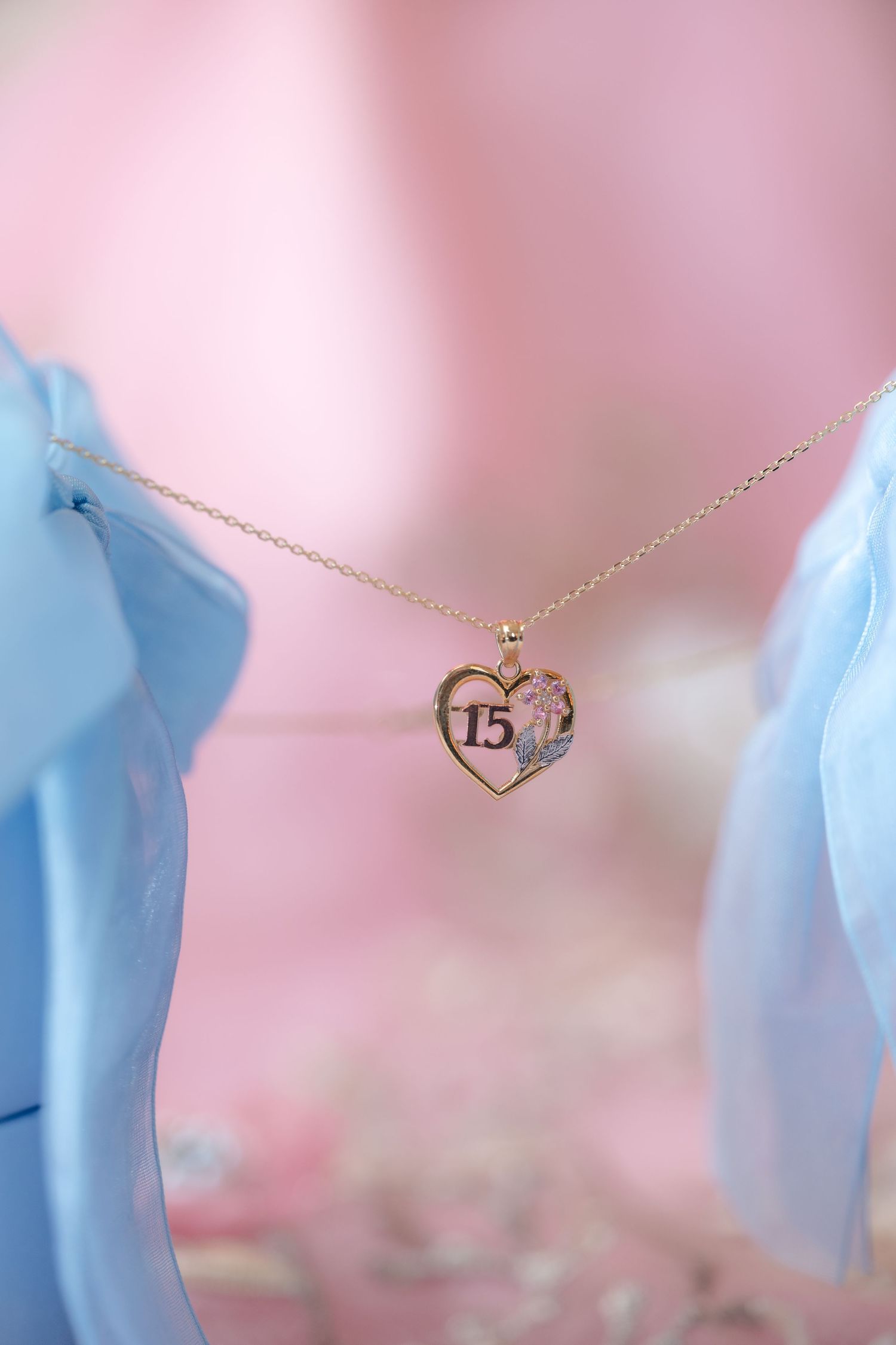 Delicate gold necklaces with charms displayed against a soft pink and blue background.