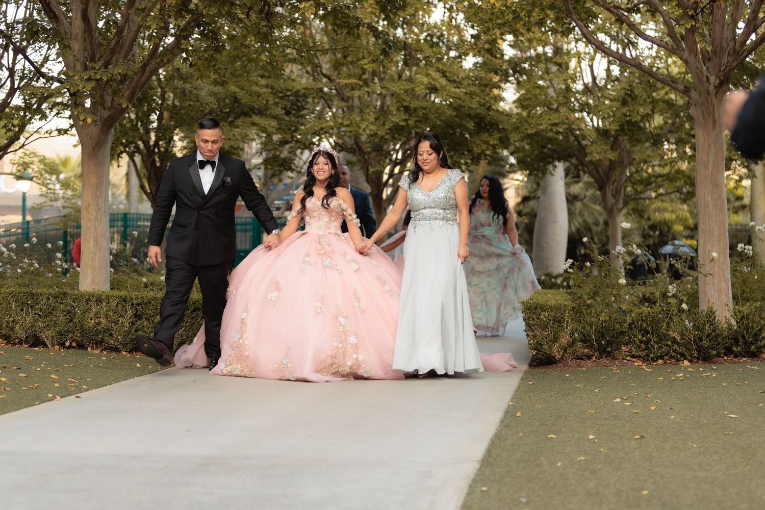 Wedding party poses outdoors in formal attire with pink and blue dresses against a garden backdrop at sunset.