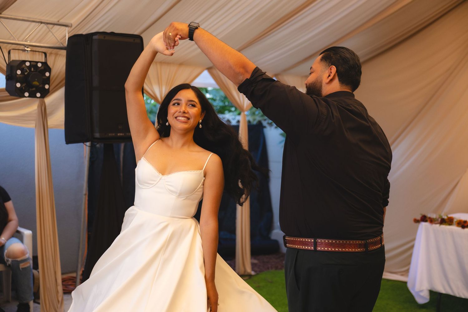 A couple dances together under a white tent at their wedding celebration.