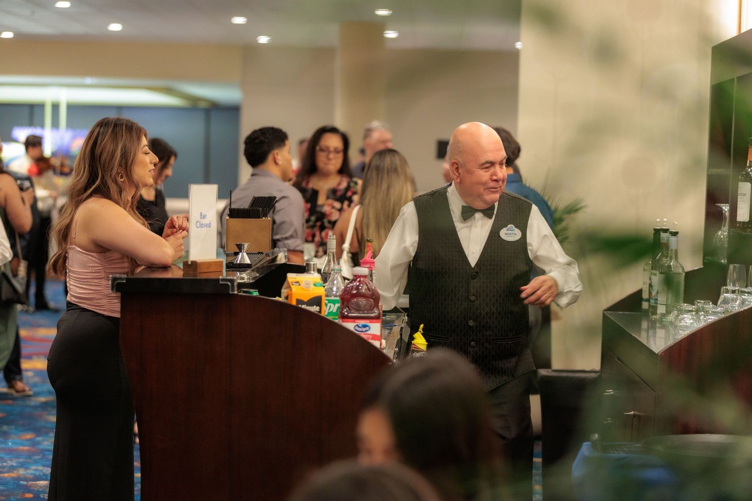Guests mingling at an elegant reception around a dark wooden bar area.