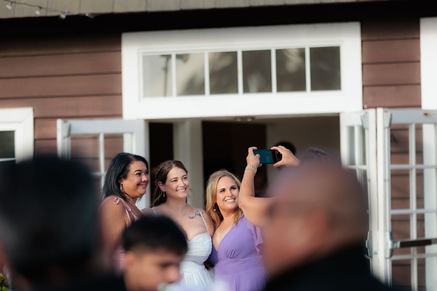 A group of people stand outside a white-trimmed brown building looking up at something in the sky.