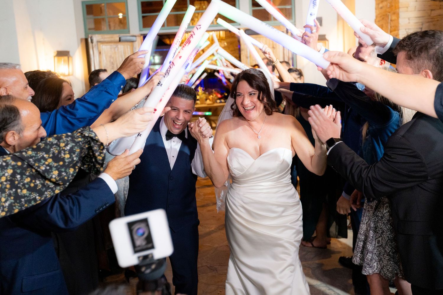 Wedding guests create a dance tunnel at a reception as the newlyweds dance through with raised arms in celebration.