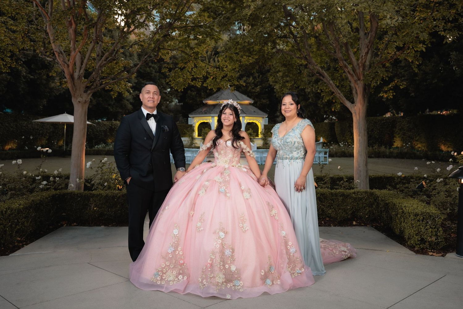 Formal celebration outdoors with pink quinceañera gowns and light blue bridesmaid dresses.