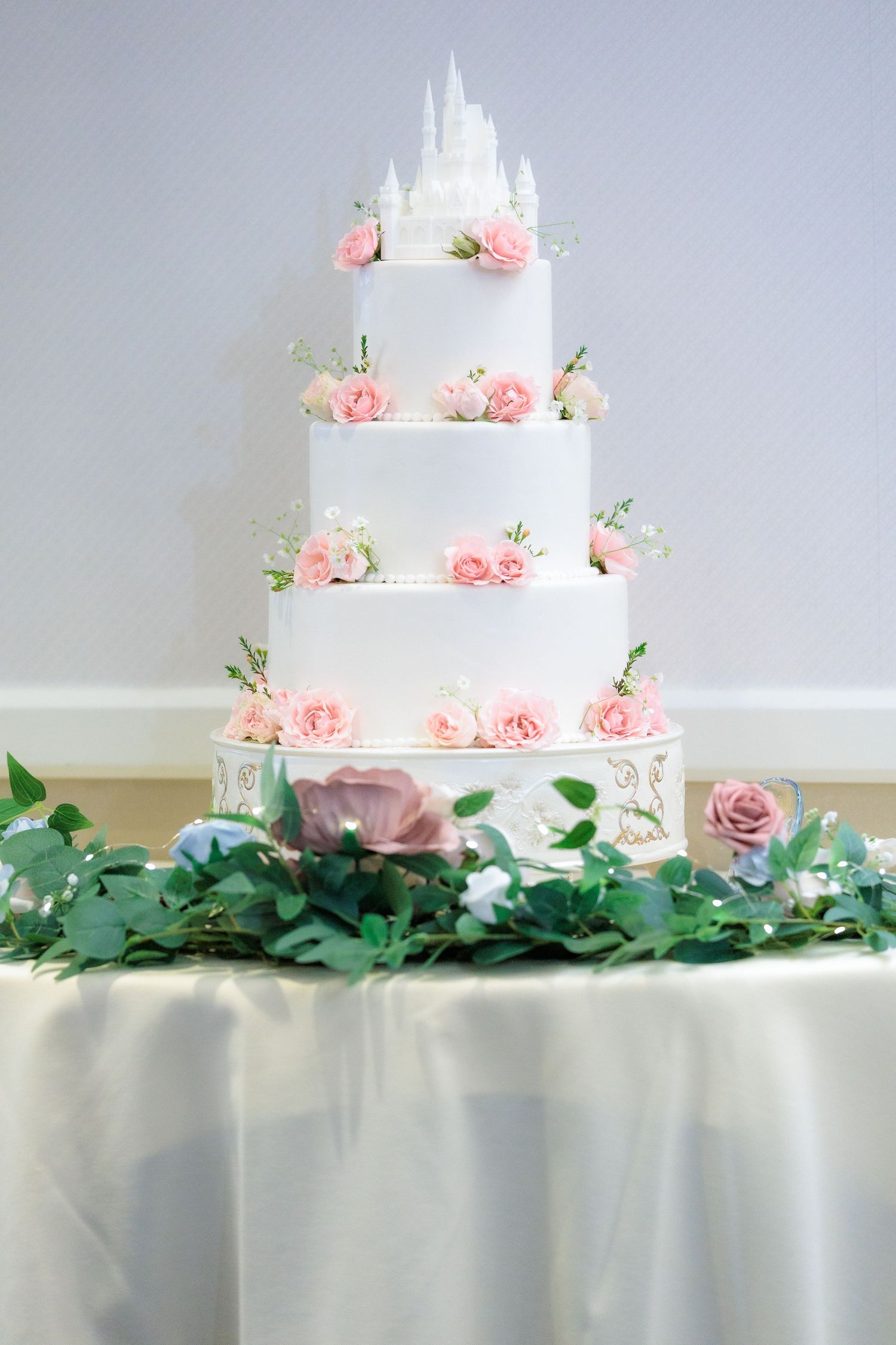 A three-tiered white wedding cake decorated with delicate pink roses and green foliage on a white tablecloth.