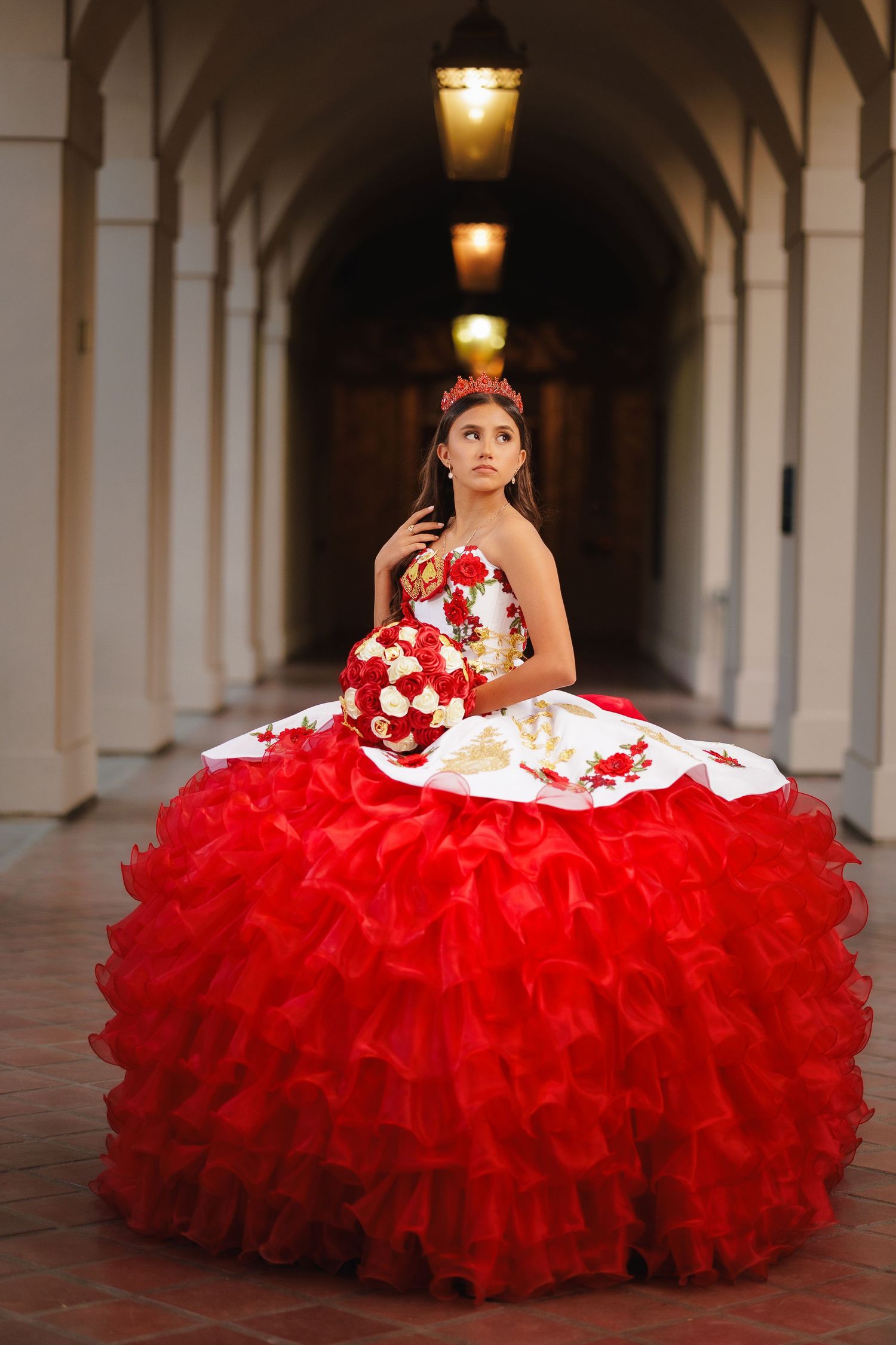 A stunning red and white quinceanera dress with ruffled tulle skirt photographed in an elegant arched hallway.