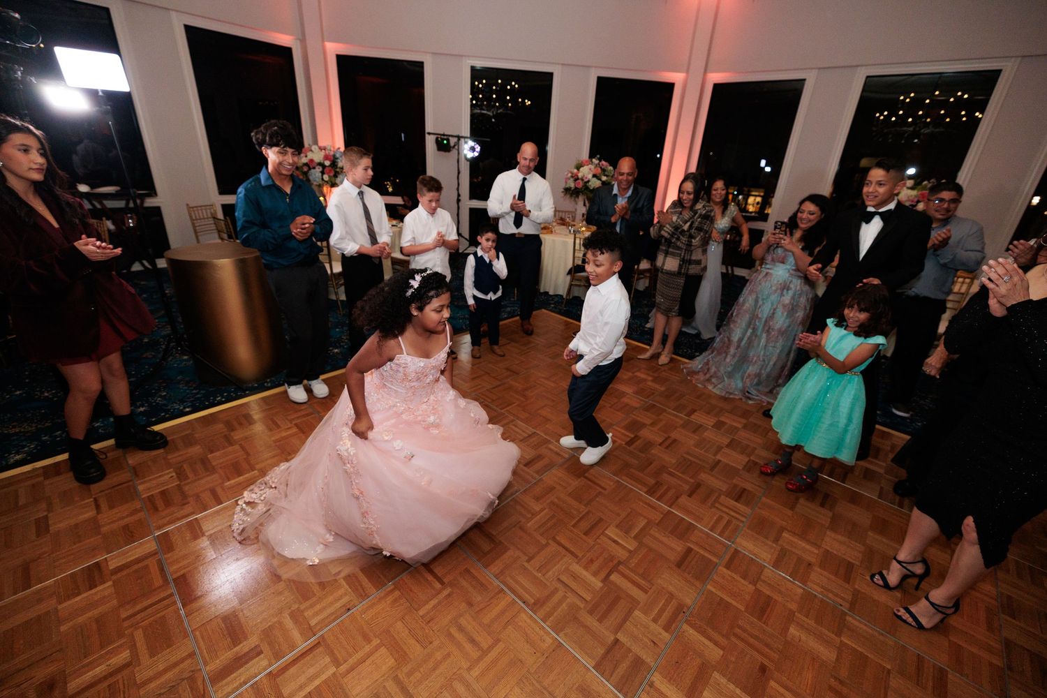 Wedding reception guests dance on a parquet floor under ambient lighting in an elegant venue.