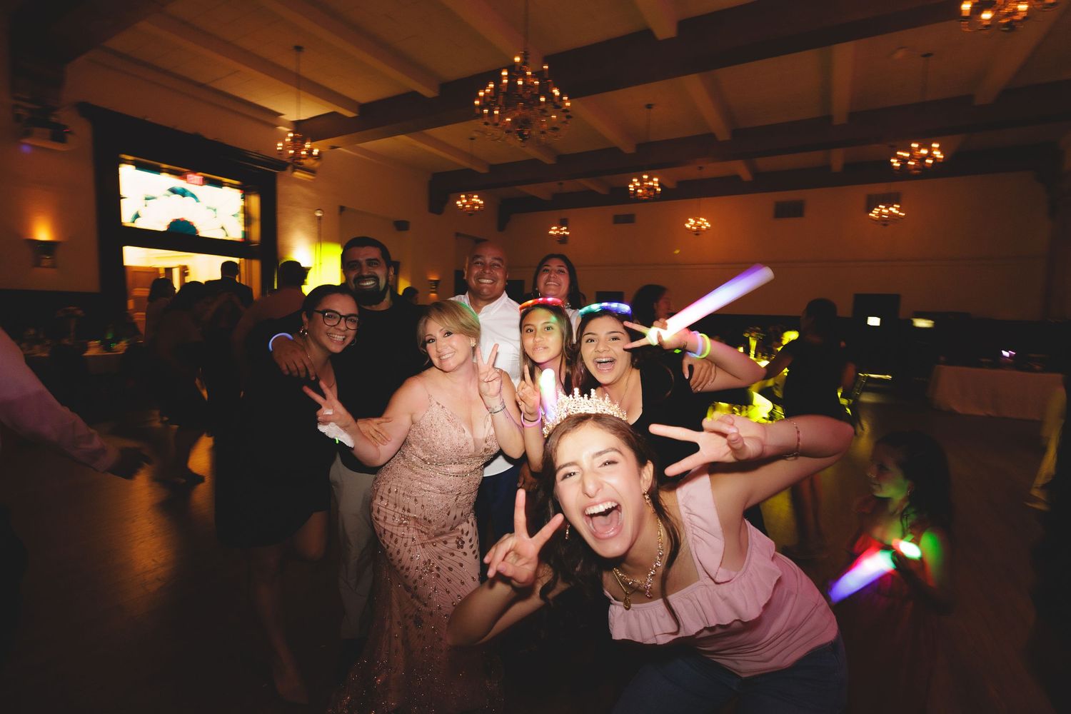 People dancing and celebrating at a dimly lit reception venue with festive lighting and decorations.