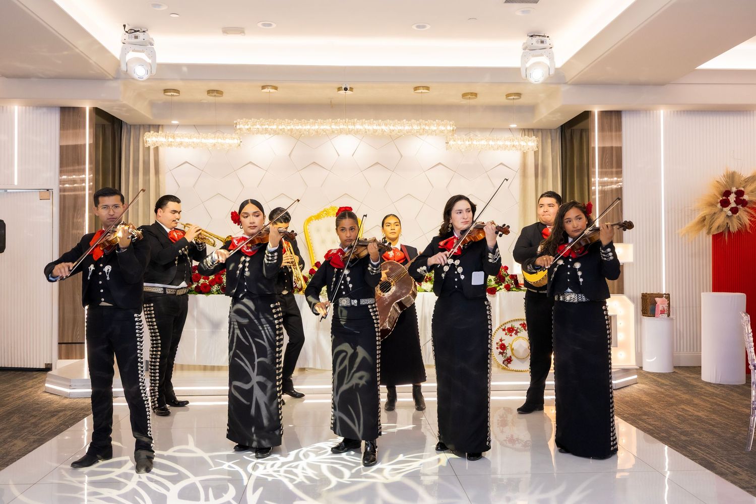 Wedding party in formal black attire performs choreographed dance routine in elegant white ballroom.