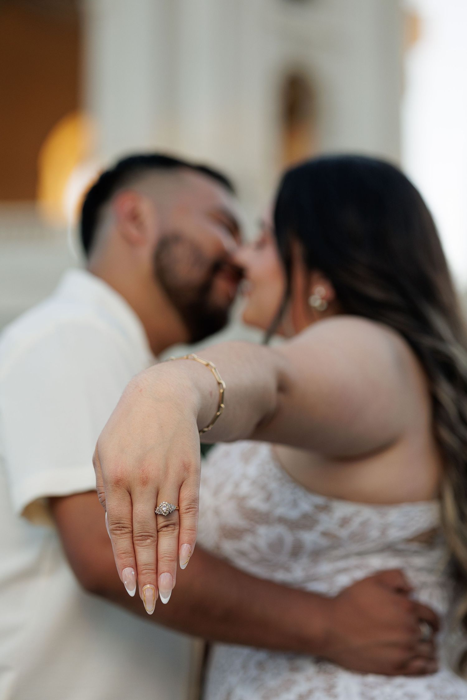 A close-up shot of a couple embracing shows the bride's hand with an engagement ring and delicate bracelet.