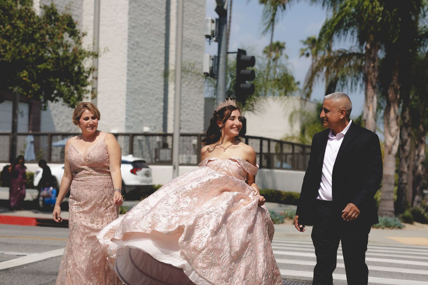A wedding party poses together outdoors in coordinated pink and blush formal attire on a sunny day.