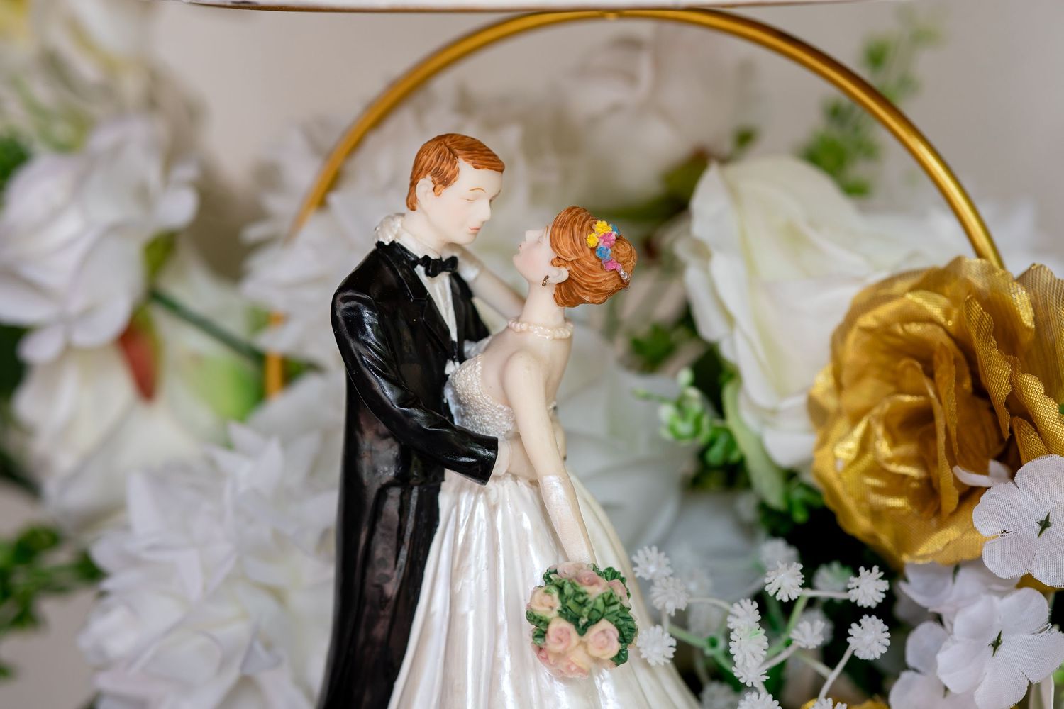 Wedding cake topper figurines arranged with white and gold floral decorations on an elegant display.