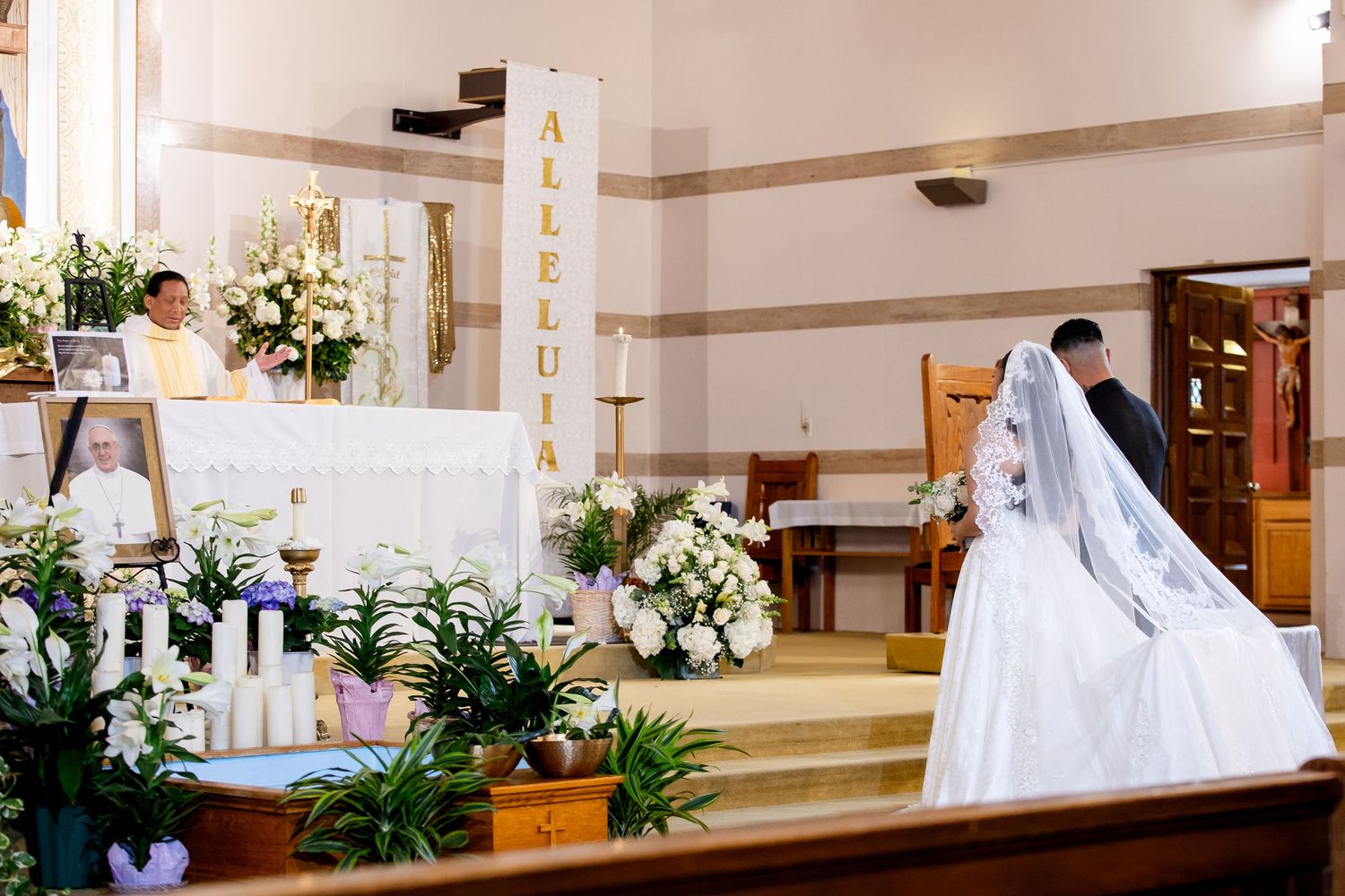 Wedding ceremony setup in a church sanctuary with white pews, floral arrangements, and traditional decor.