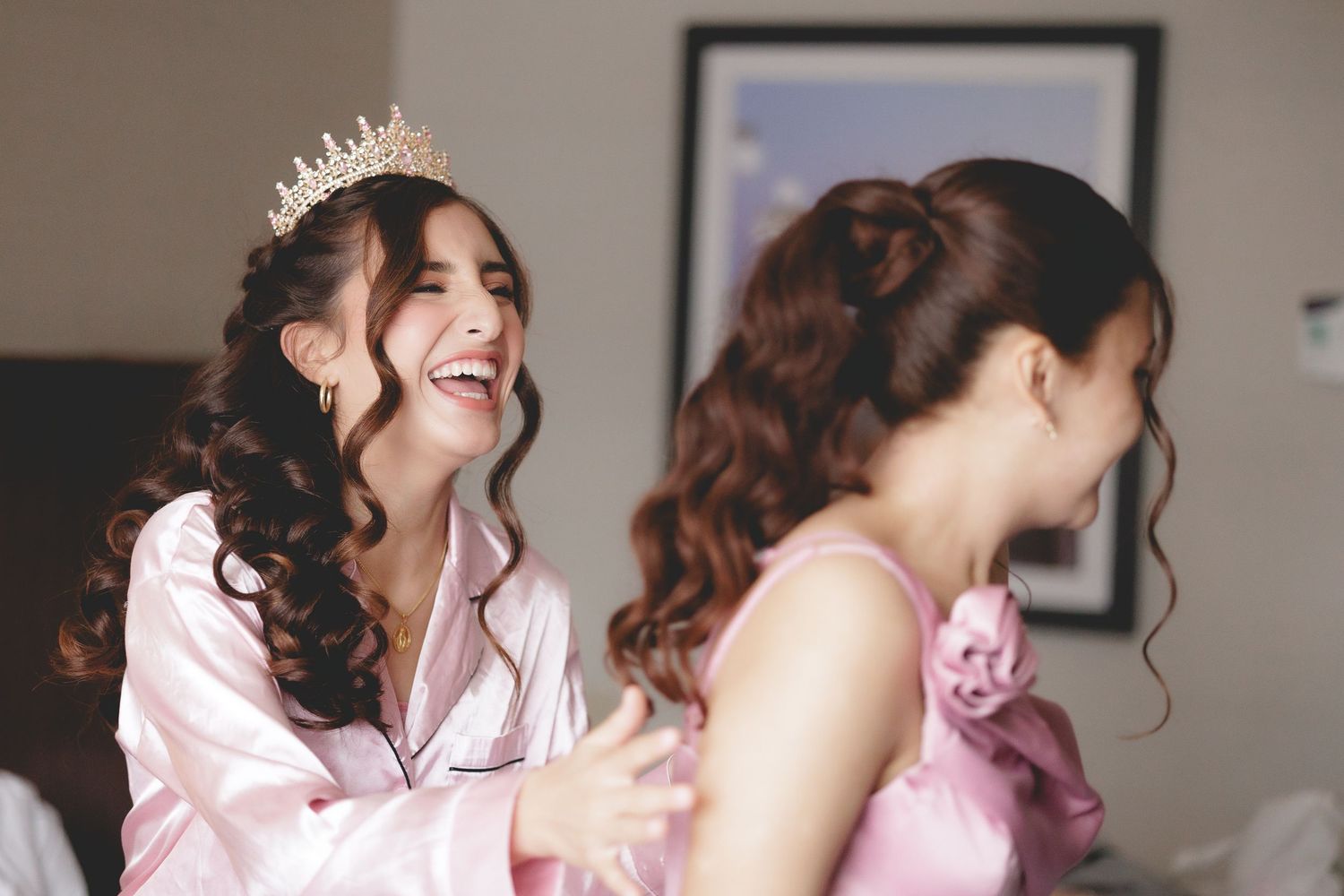 Two women in pink share a joyful moment during pre-wedding preparations, with one wearing a delicate tiara.