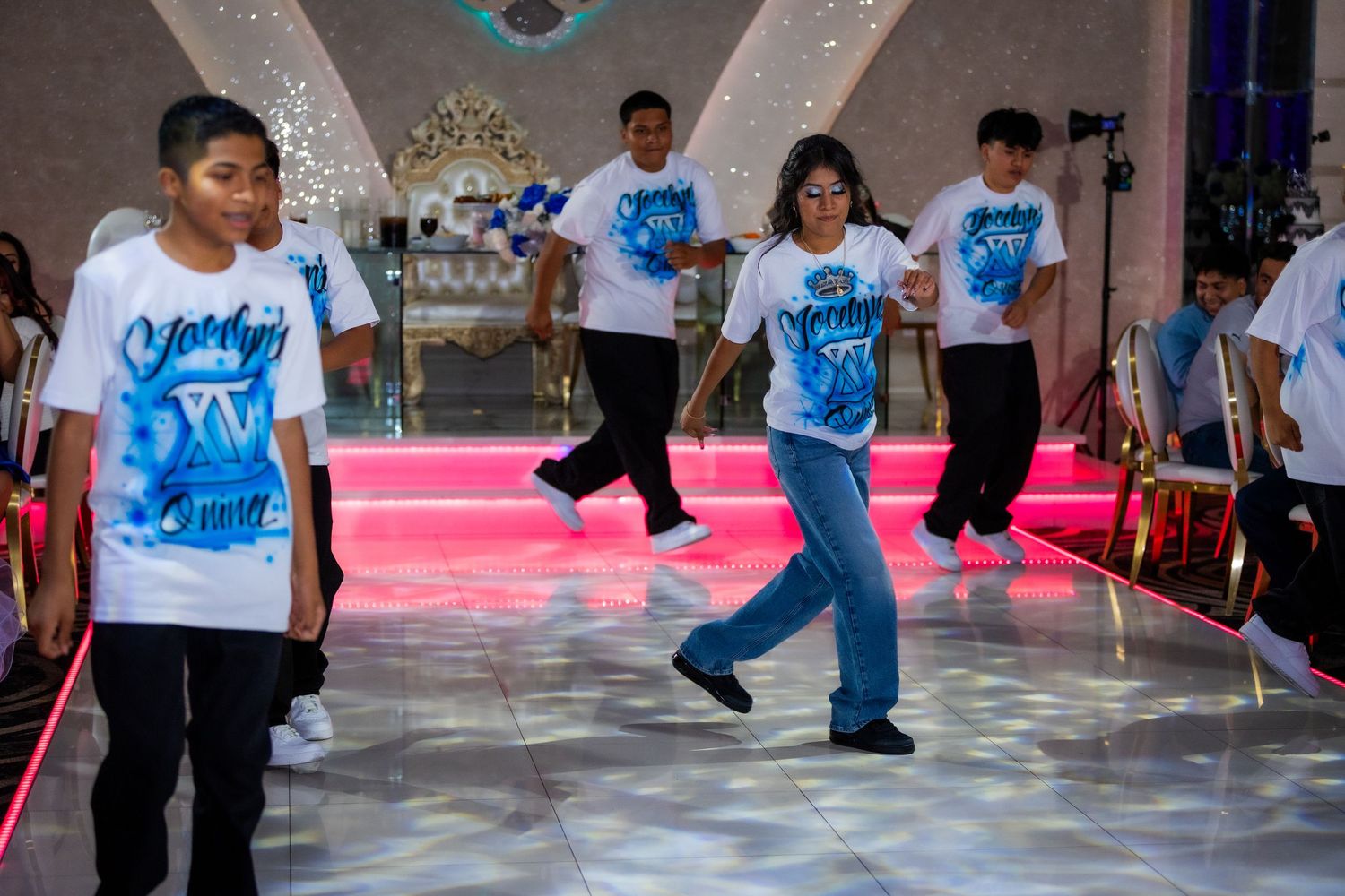 Breakdancers in light blue shirts perform dynamic dance moves on a polished floor during a competition event.
