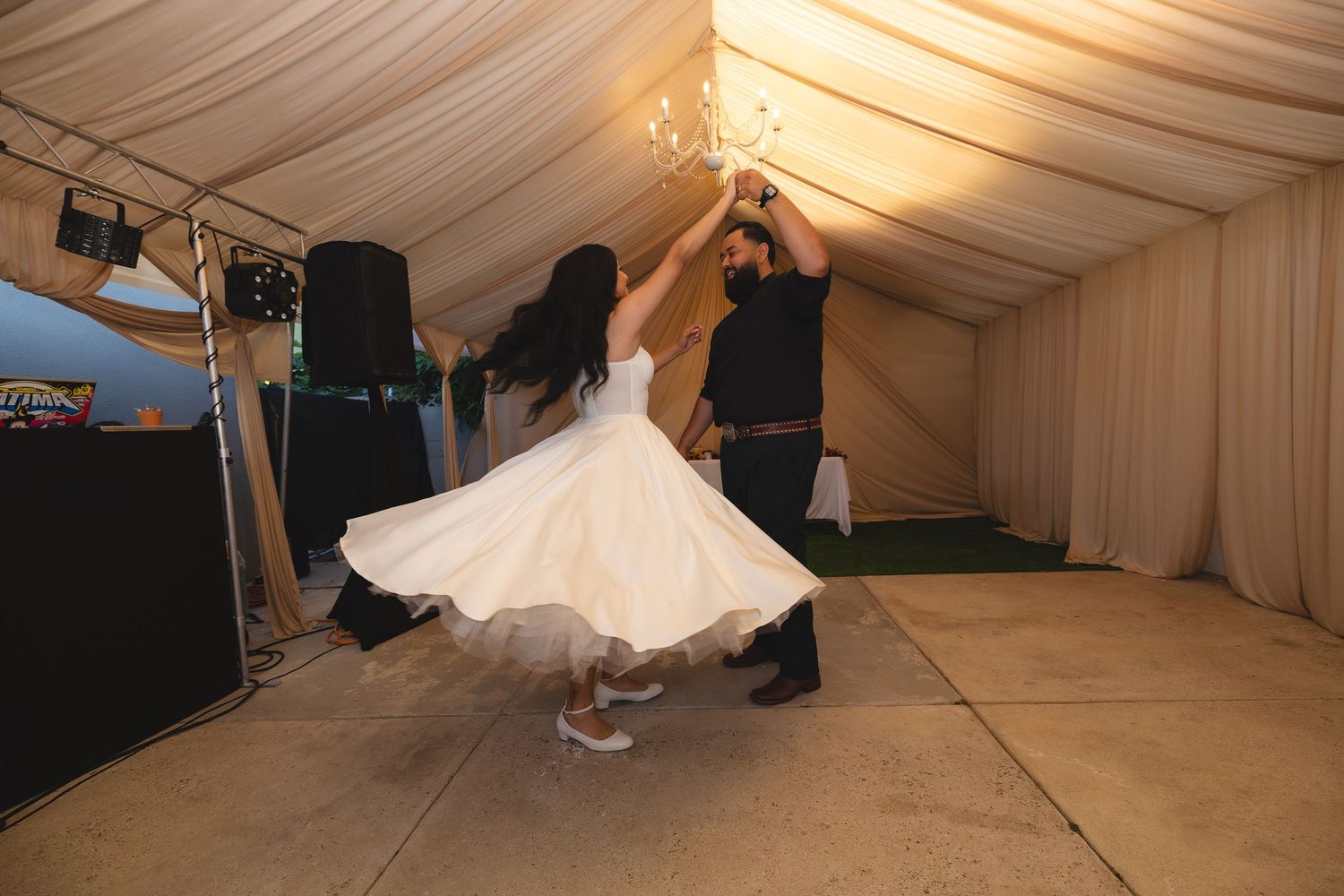 A bride in a flowing white wedding dress twirls and dances under an elegant white tent canopy.