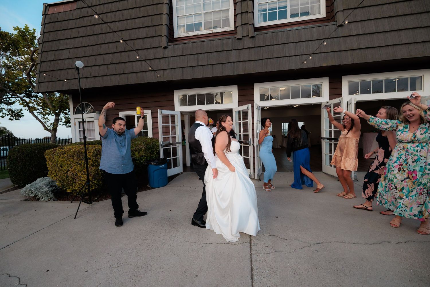 Wedding party guests dance together during an outdoor reception at a rustic barn venue.
