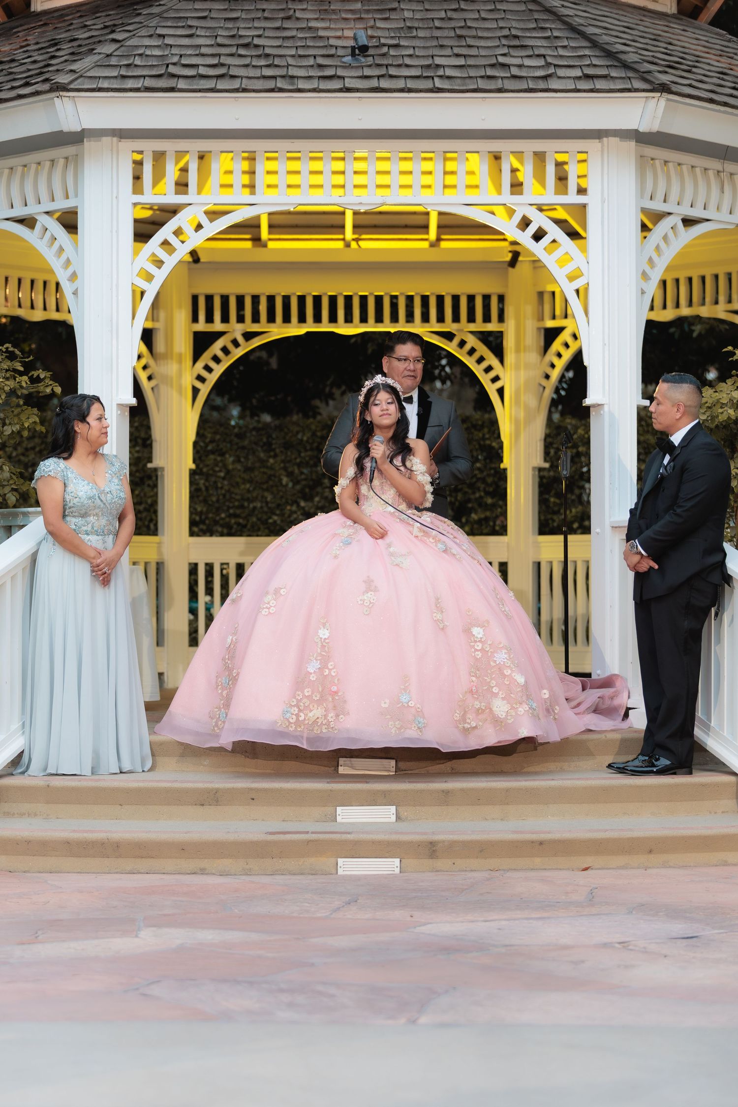 A pink ballgown dress being showcased in a series of poses under a white and yellow gazebo.