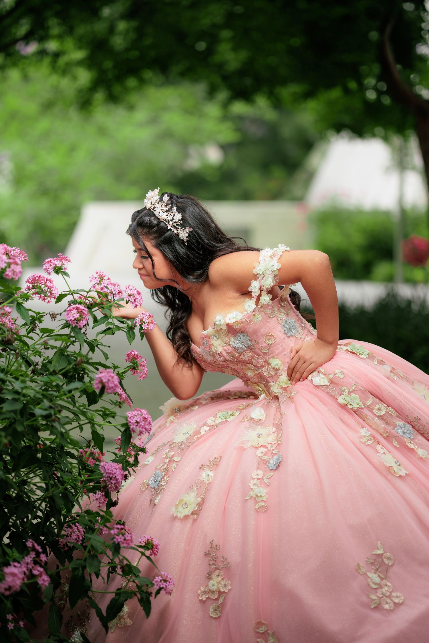 A pink ballgown with floral embellishments is photographed in a garden setting with blooming pink flowers.